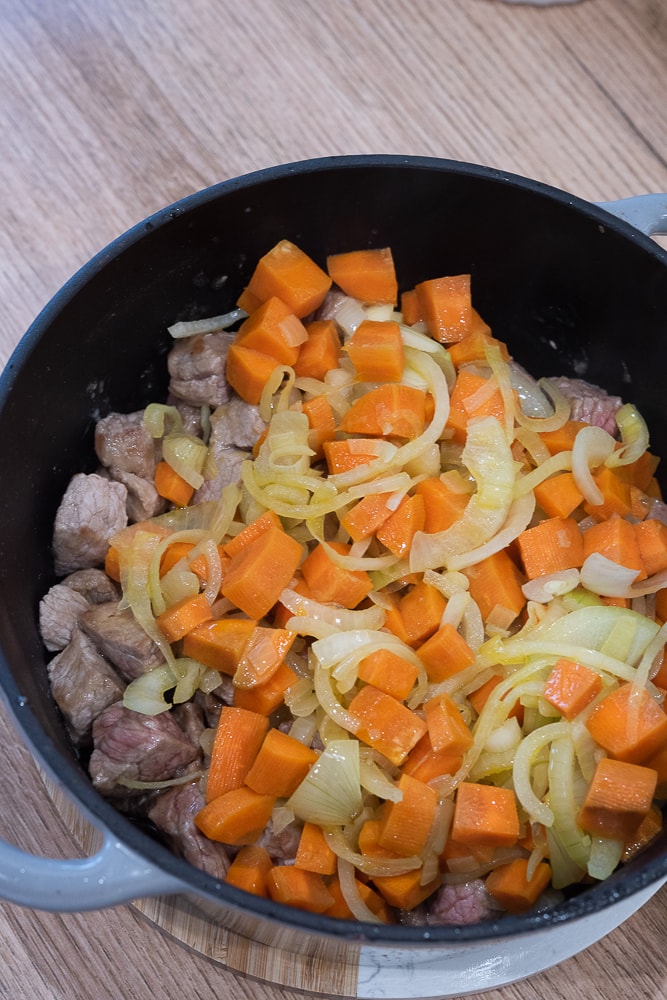 Wołowina pokrojona w kostkę wraz z podsmażoną cebulką i marchewką w garnku żeliwnym